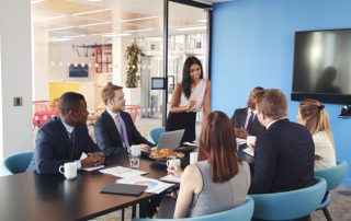 Female manager stands addressing colleagues in meeting room