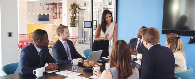 Female manager stands addressing colleagues in meeting room
